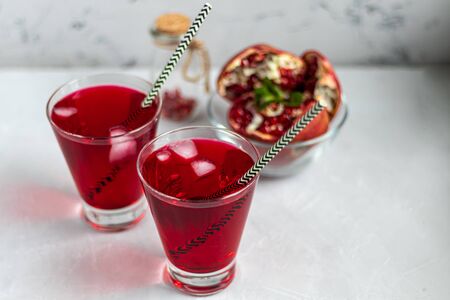 Pomegranate juice in transparent glasses. On a light background under a stone. Trend 2020. Grains are scattered nearby. Copy space.の写真素材