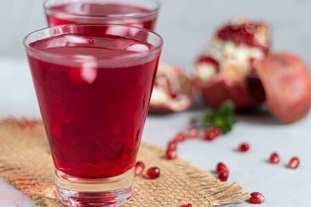 Pomegranate juice in transparent glasses. On a light background under a stone. Trend 2020. Grains are scattered nearby. Copy space.の写真素材