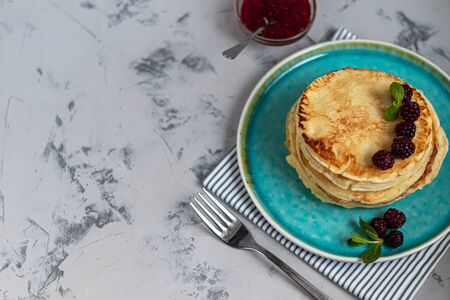 A stack of delicious pancakes with raspberries, blackberries and blueberries. On a light background. Sprinkled with icing sugar and decorated with mint leaves. Copy space.の写真素材