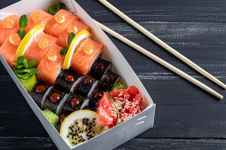 A box of sushi Nigiri, Uramaki California, Philadelphia, on a black stone plate. Sushi menu in a white transport box on a wooden background. Copy space.の写真素材