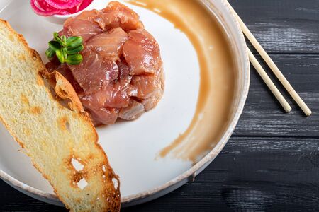 Salt marinated silver carp, diced, next to onion marinated in wine vinegar, fried croutons. Decorated with microgreen. On a wooden background. Copy spaceの写真素材
