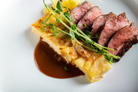 Duck breast with a side dish of potato casseroles, seasoned with pea microgreen with tomato and...