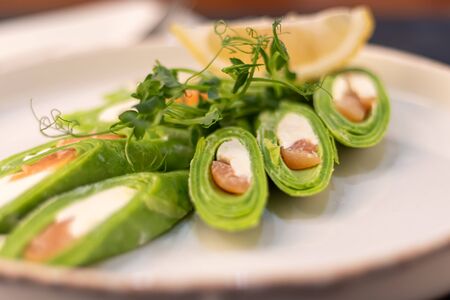 Spinach rolls. Dressed with cheese, red fish. Garnished with sprigs of microgreen, a slice of lemon. On a wooden natural background. Copy spaceの写真素材