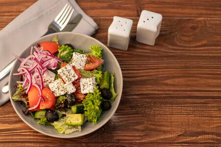 Greek vegetable salad. It consists of tomatoes, olives, feta cheese, herbs, cucumbers and red onions. On a wooden background. Copy spaceの写真素材