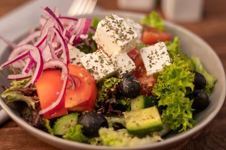 Greek vegetable salad. It consists of tomatoes, olives, feta cheese, herbs, cucumbers and red onions. On a wooden background.の写真素材