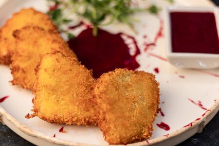 Camembert cheese fried in batter and breadcrumbs with cranberry sauce. Soft and viscous inside. The plate is decorated with a spray of sauce and microgreen. On a wooden background. Copy spaceの写真素材