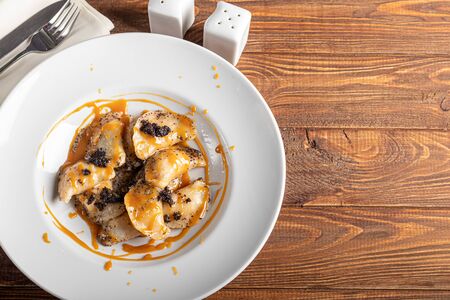 Ravioli stuffed with cottage cheese and poppy seeds. Served with poppy seeds and caramel sauce. On a large white plate. On a wooden background. Copy spaceの写真素材