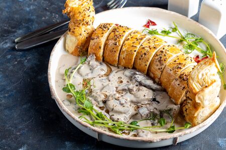 Puff pastry roll stuffed with mushrooms. Nearby are champignons in sour cream, sliced. Served with microgreen and sun-dried tomatoes. On a dark background. Copy spaceの写真素材