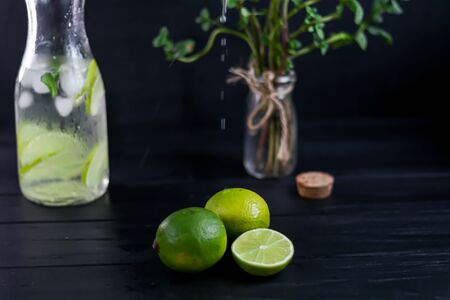 Fresh ripe limes on a wooden background. In the background is a drink and mint branches. Copy spaceの写真素材