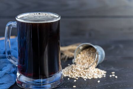 Homemade dark beer in bottles and a glass on a dark background. Nearby are barley grains and ears of wheat. Dark background. Copy spaceの写真素材