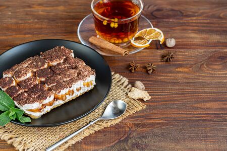 Tiramisu. Traditional italian dessert on wooden background. Garnished with a sprig of mint, lime slices. In a transparent cup, tea with sea buckthorn. Copy spaceの写真素材