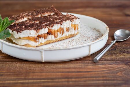 Tiramisu. Traditional italian dessert on wooden background. Garnished with a sprig of mint, lime slices. In a transparent cup, tea with sea buckthorn. Copy spaceの写真素材