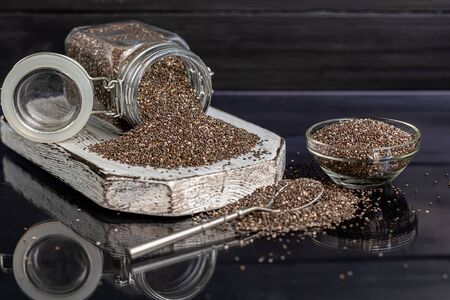 Black chia seeds in glassware contain healthy vitamins and minerals. On a black background with a metal spoon. Copy spaceの写真素材