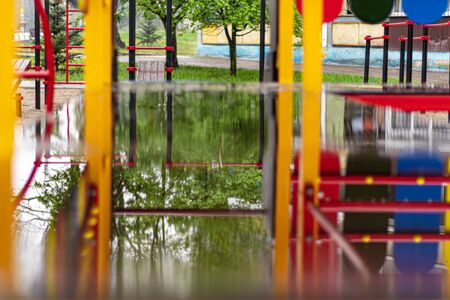 Empty swing at the playground in the rain. Children's swing in the park, wooden benches, slides, sports equipment. Empty city, quarantine. The concept of loneliness.の写真素材