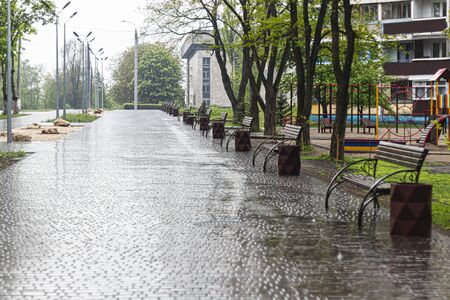 Empty swing at the playground in the rain. Children's swing in the park, wooden benches, slides, sports equipment. Empty city, quarantine. The concept of loneliness.の写真素材