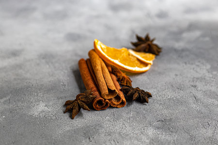 Cinnamon sticks, anise stars and nutmeg on a gray background. Near slices of chips from an orange....