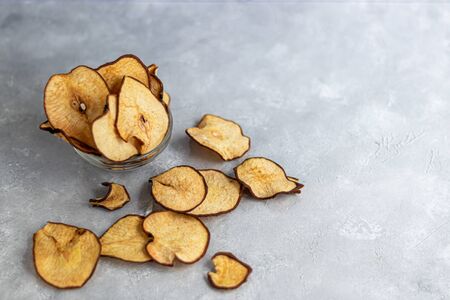 Crispy pear fruit chips on a gray background. In the background are ripe pears. Healthy food, decor. Copy spaceの写真素材
