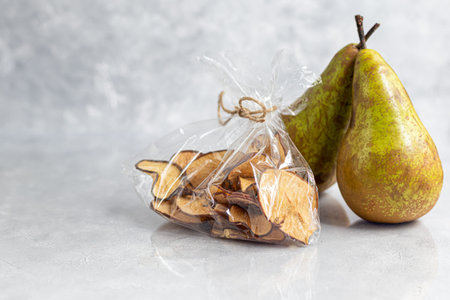 Crispy pear fruit chips on a gray background. In the background are ripe pears. Healthy food, decor. Copy spaceの写真素材