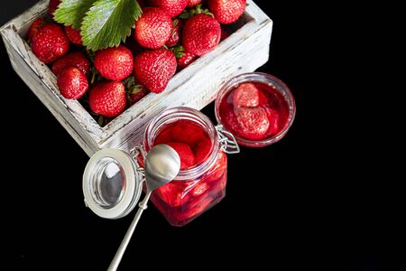 Strawberry jam in a glass jar next to fresh strawberries. On a black wooden background. Homemade winter fruit blanks. Selective focus. Copy spaceの写真素材