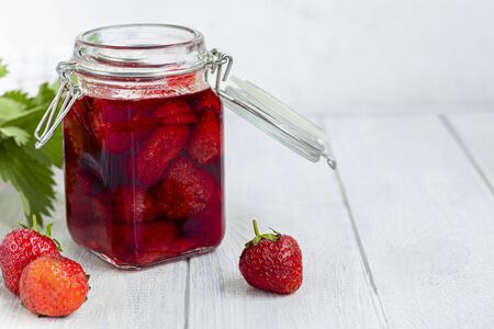 Strawberry jam in a glass jar next to fresh strawberries. On a white wooden background. Homemade winter fruit blanks. Selective focus. Copy spaceの写真素材