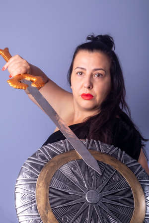 Portrait of a European woman with a shield and sword in her hands. Shooting in the studio. Close-up, red lipstick, model in black dress.の写真素材