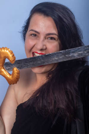 Portrait of a European woman with a sword in her hands. Shooting in the studio. Close-up, red lipstick, model in a black cape.の写真素材