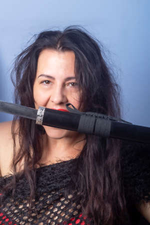 Portrait of a European woman with a sword in her hands. Shooting in the studio. Close-up, red lipstick, model in a black cape.の写真素材