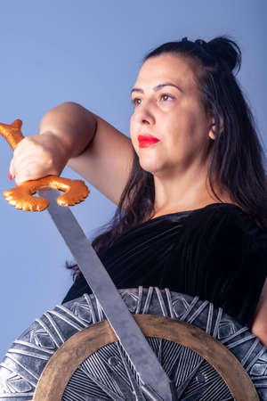 Portrait of a European woman with a shield and sword in her hands. Shooting in the studio. Close-up, red lipstick, model in black dress.の写真素材