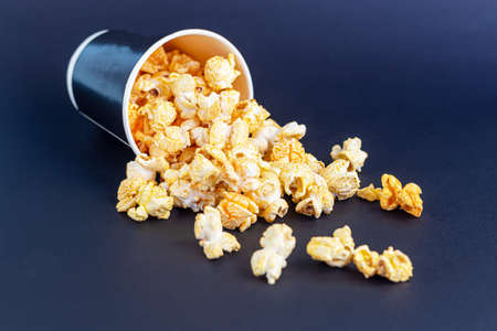 Paper cup with popcorn on the dark surface. Nearby is a mask and headphones. Watching movies in quarantine. Copy space.の写真素材