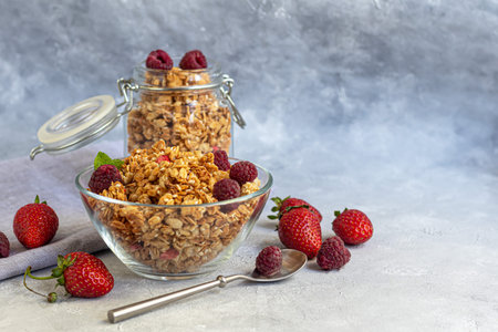 Homemade granola with strawberry slices in a glass jar. On a gray background. Vegetarian dish....