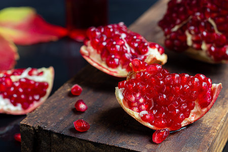 Large pomegranate, broken into pieces. On a dark background. Grains are scattered nearby. Autumn...