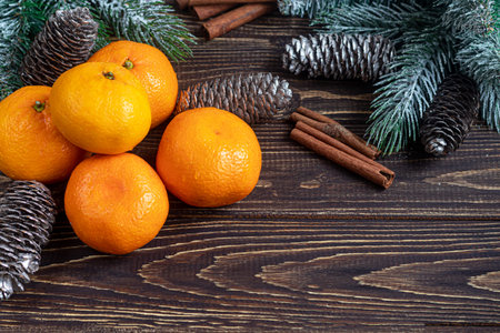 Tangerines on a wooden background with branches of a Christmas tree and pine cones covered with...