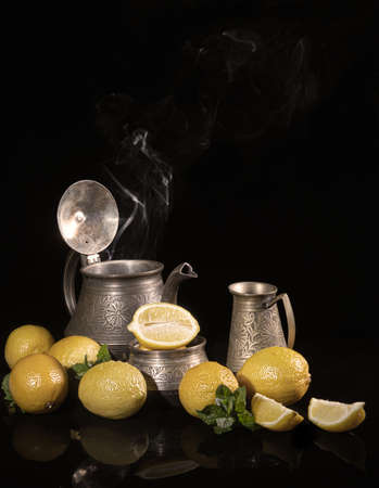 Tea with lemons. Still life of lemons and metal dishes, a teapot, a milk jug and a sugar bowl. Decorated with mint. Copy space.の写真素材