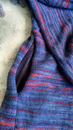 Handmade knitted products. Knitted cardigan made of purple and red threads. Gray background. Copy...