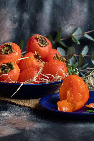 Persimmon on a dark background. Fresh, ripe fruits on a blue plate and in a box. Healthy eating.の写真素材