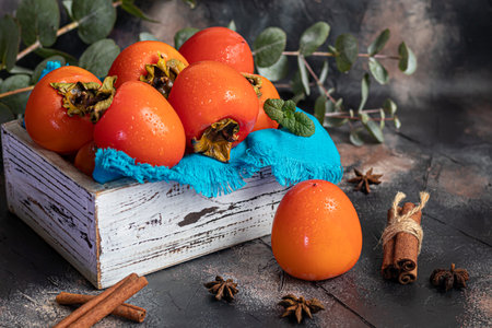 Persimmon on a dark background. Fresh, ripe fruits on a blue plate and in a box. Healthy eating.の写真素材