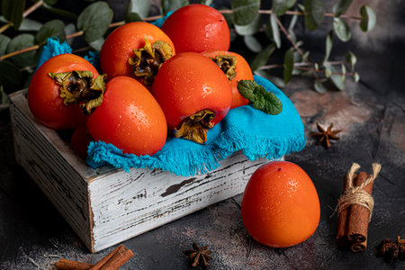 Persimmon on a dark background. Fresh, ripe fruits on a blue plate and in a box. Healthy eating.の写真素材