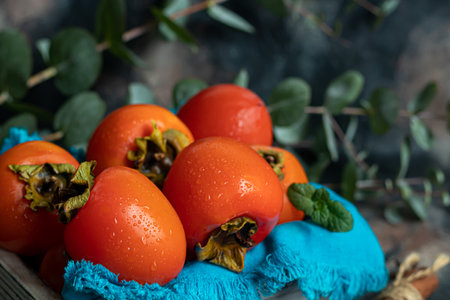 Persimmon on a dark background. Fresh, ripe fruits on a blue plate and in a box. Healthy eating.の写真素材