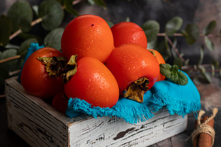 Persimmon on a dark background. Fresh, ripe fruits on a blue plate and in a box. Healthy eating.の写真素材