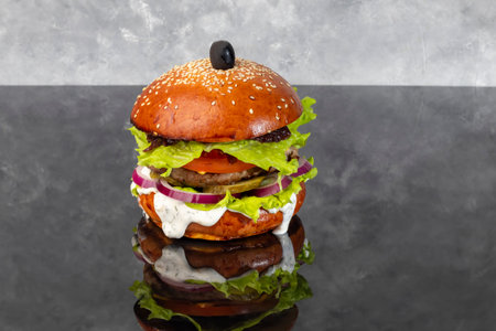 Burger on a wooden board with a patty, tomato, cheese, cucumber and lettuce. Glass of beer in the background. Copy spaceの写真素材