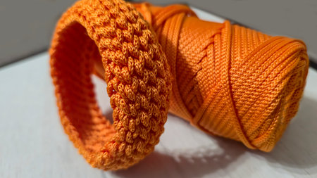 Orange bracelet crocheted from cord on gray background. Handmade trend.