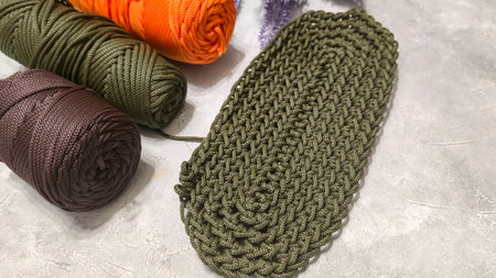 Crochet bag bottom made of green polyester cord. On a gray background. Textured design