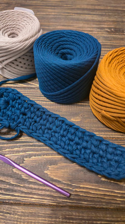 The bottom of the bag is crocheted from blue knitted yarn. On a wooden background. Handmade.