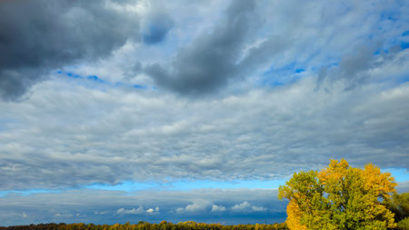An autumn river landscape with yellow leaves on the trees, reflections, and a blue sky. City beach. Lots of clouds. Tourism.の写真素材