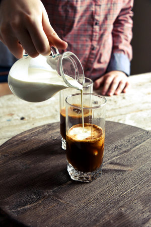 Coffee in a glass. The cream in the jar. Hands