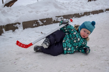 The little boy was tired of playing hockey and went to rest on the snow with a stick in winter in a snow-covered park.の写真素材