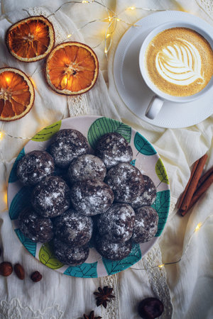 Chocolate gingerbread sprinkled with powdered sugar on a plate with turquoise leaves, dried oranges,...