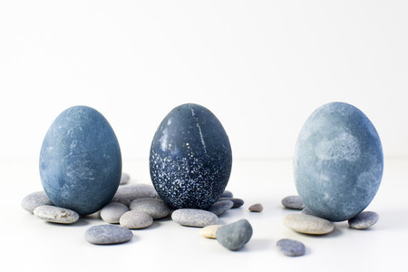 Three colored blue, gray marble eggs stand vertically among the stones on a white backgroundの写真素材