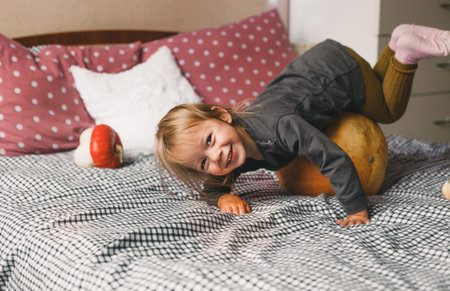 a little girl has fun having fun and laughing, riding a big pumpkin in a cozy house on her bed.の写真素材