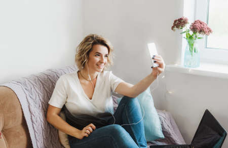 a young girl blogger leads an online broadcast communicates with her subscribers sitting at home on the couch in a cozy atmosphereの写真素材